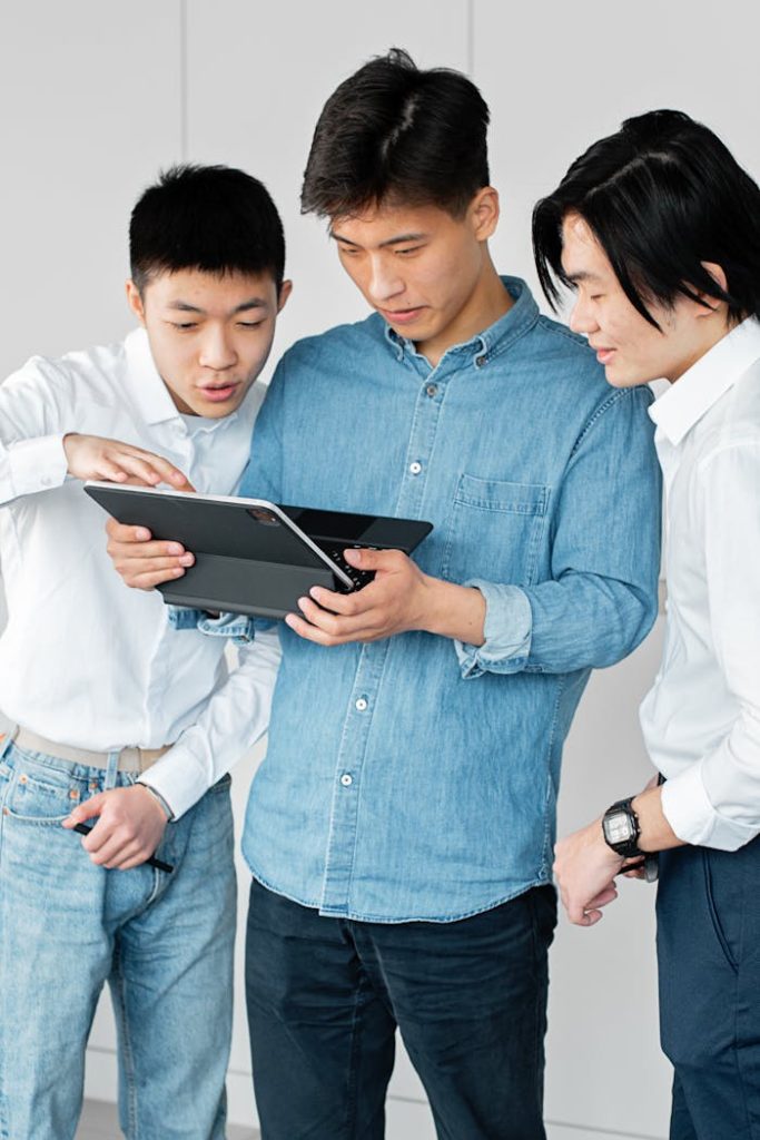 Three young men discussing work on a tablet in a modern office setting.